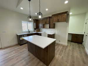 Kitchen featuring sink, decorative light fixtures, a center island, stainless steel dishwasher, and light hardwood / wood-style floors