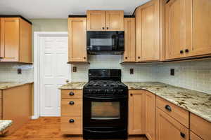 Kitchen featuring light stone counters, light hardwood / wood-style floors, decorative backsplash, and black appliances