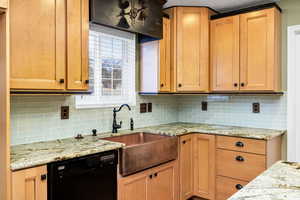 Kitchen featuring tasteful backsplash, sink, light stone countertops, and black dishwasher