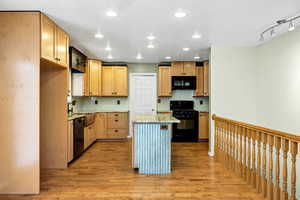 Kitchen with light wood-type flooring, a kitchen island, light stone countertops, decorative backsplash, and black appliances