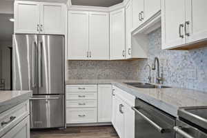 Kitchen featuring sink, white cabinets, backsplash, stainless steel appliances, and light stone countertops