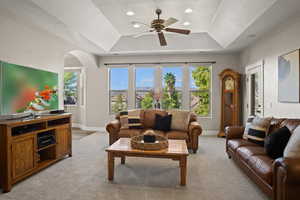 Living room with a wealth of natural light, a raised ceiling, and ceiling fan