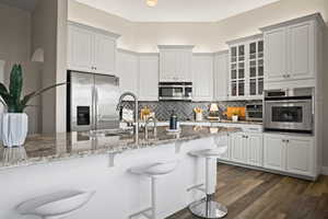 Kitchen featuring white cabinetry, appliances with stainless steel finishes, a kitchen bar, and light stone counters