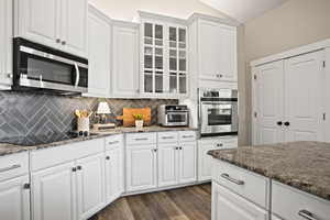 Kitchen featuring white cabinetry, stainless steel appliances, dark hardwood / wood-style floors, tasteful backsplash, and dark stone counters