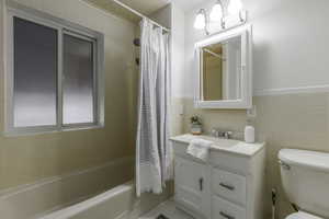 Full bathroom featuring shower / bath combo, tile walls, vanity, and toilet