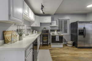 Kitchen featuring appliances with stainless steel finishes, white cabinetry, rail lighting, sink, and light wood-type flooring