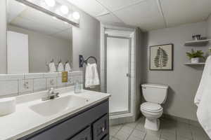 Bathroom with a shower with door, vanity, a paneled ceiling, and toilet