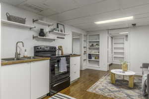 Kitchen featuring sink, a paneled ceiling, hardwood / wood-style flooring, black range with electric stovetop, and white cabinets