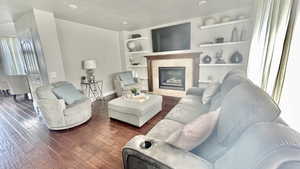 Living room featuring built in features, a fireplace, hardwood / wood-style floors, and a textured ceiling