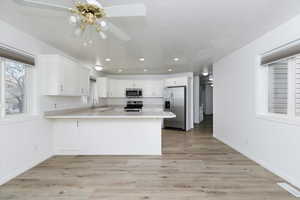 Kitchen with appliances with stainless steel finishes, white cabinetry, sink, kitchen peninsula, and light hardwood / wood-style flooring