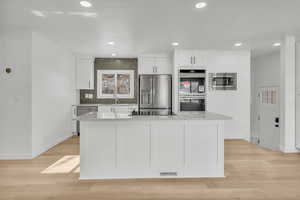 Kitchen featuring appliances with stainless steel finishes, a center island, light stone countertops, and white cabinets