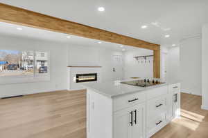 Kitchen featuring white cabinetry, light stone counters, light hardwood / wood-style flooring, black electric stovetop, and beam ceiling