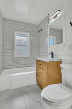 Full bathroom featuring vanity, tiled shower / bath, tile walls, and toilet