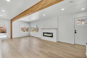 Unfurnished living room with beamed ceiling, a large fireplace, and light hardwood / wood-style flooring