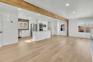 Kitchen featuring a kitchen island, beamed ceiling, white cabinets, stainless steel appliances, and light wood-type flooring