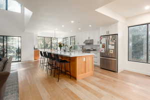 Kitchen with decorative light fixtures, stainless steel refrigerator, white cabinets, a large island, and backsplash