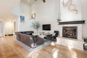 Living room featuring a stone fireplace, light hardwood / wood-style flooring, ceiling fan, and a towering ceiling