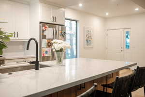 Kitchen featuring white cabinets, light stone countertops, a breakfast bar, and stainless steel refrigerator