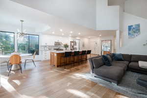 Living room with sink, a chandelier, light wood-type flooring, a tray ceiling, and a towering ceiling