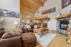 Living room featuring a fireplace, a chandelier, light hardwood / wood-style floors, wooden ceiling, and beam ceiling