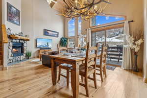 Dining space with an inviting chandelier, a stone fireplace, light hardwood / wood-style floors, and a high ceiling