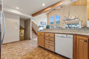 Kitchen featuring lofted ceiling with beams, stainless steel fridge, hanging light fixtures, light stone counters, and white dishwasher