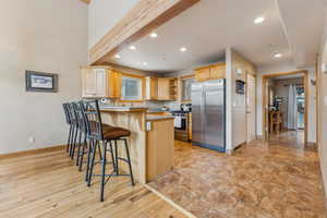 Kitchen with a breakfast bar, appliances with stainless steel finishes, beam ceiling, light brown cabinetry, and kitchen peninsula