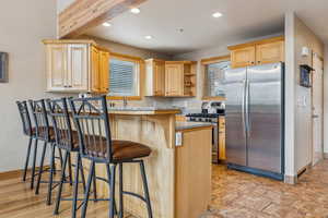 Kitchen featuring stainless steel appliances, a kitchen breakfast bar, a center island, light stone countertops, and light brown cabinets