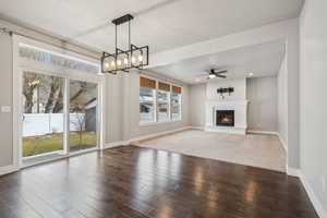 Unfurnished living room featuring ceiling fan with notable chandelier and dark hardwood / wood-style floors