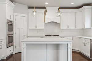 Kitchen featuring white cabinetry, appliances with stainless steel finishes, decorative light fixtures, and custom exhaust hood