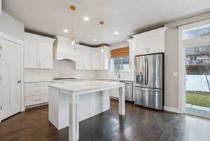 Kitchen with white cabinetry, hanging light fixtures, stainless steel appliances, a center island, and custom range hood