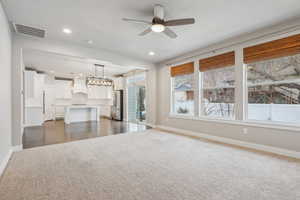 Unfurnished living room featuring ceiling fan with notable chandelier and dark carpet