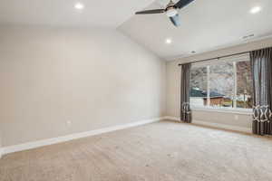 Empty room with ceiling fan, vaulted ceiling, and light carpet