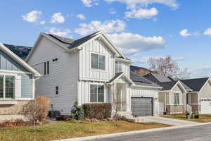 View of front of home with a garage, central air condition unit, a front yard, and solar panels