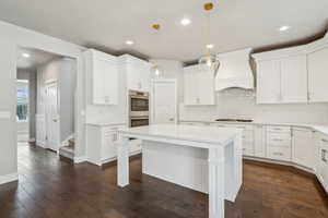 Kitchen featuring pendant lighting, dark wood-type flooring, premium range hood, white cabinets, and a kitchen island