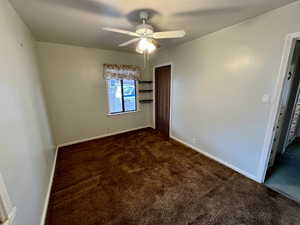 Unfurnished bedroom with ceiling fan, dark carpet, and a closet