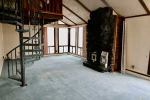 Unfurnished living room with carpet flooring, vaulted ceiling with beams, a textured ceiling, and a wood stove