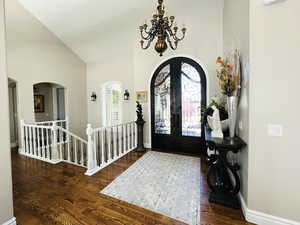 Entryway with high vaulted ceiling, dark hardwood / wood-style floors, an inviting chandelier, and french doors