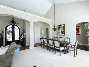 Dining space with french doors, wood-type flooring, an inviting chandelier, and high vaulted ceiling