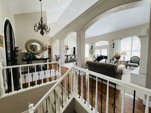 Hallway with wood-type flooring, vaulted ceiling, and an inviting chandelier