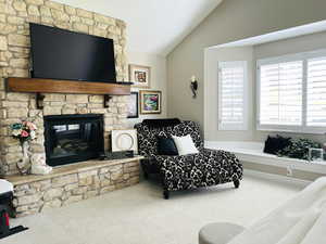 Living room featuring vaulted ceiling, a stone fireplace, and carpet floors