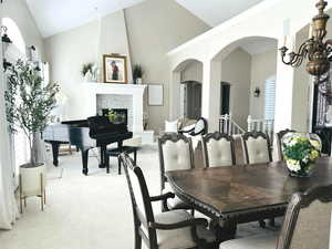 Dining room with a tiled fireplace, a healthy amount of sunlight, light colored carpet, and high vaulted ceiling