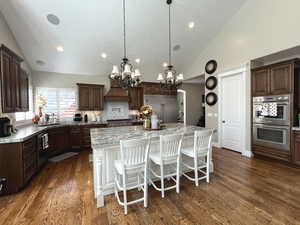 Kitchen with dark wood-type flooring, appliances with stainless steel finishes, a kitchen island, a kitchen bar, and decorative light fixtures