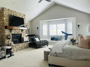 Carpeted bedroom with vaulted ceiling, a stone fireplace, and ceiling fan