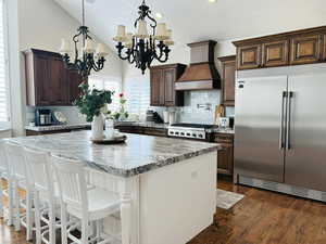 Kitchen with premium range hood, vaulted ceiling, a center island, stainless steel appliances, and an inviting chandelier