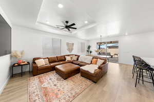 Living room with a raised ceiling, ceiling fan with notable chandelier, and light hardwood / wood-style flooring