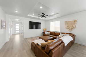 Living room featuring a raised ceiling, ceiling fan, and light hardwood / wood-style flooring