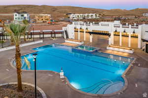 Pool at dusk featuring a community hot tub, a mountain view, and a patio area