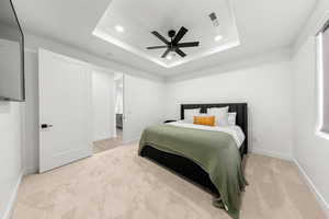 Bedroom featuring a raised ceiling, light colored carpet, and ceiling fan