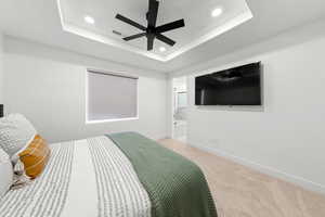 Bedroom with light carpet, connected bathroom, a raised ceiling, and ceiling fan